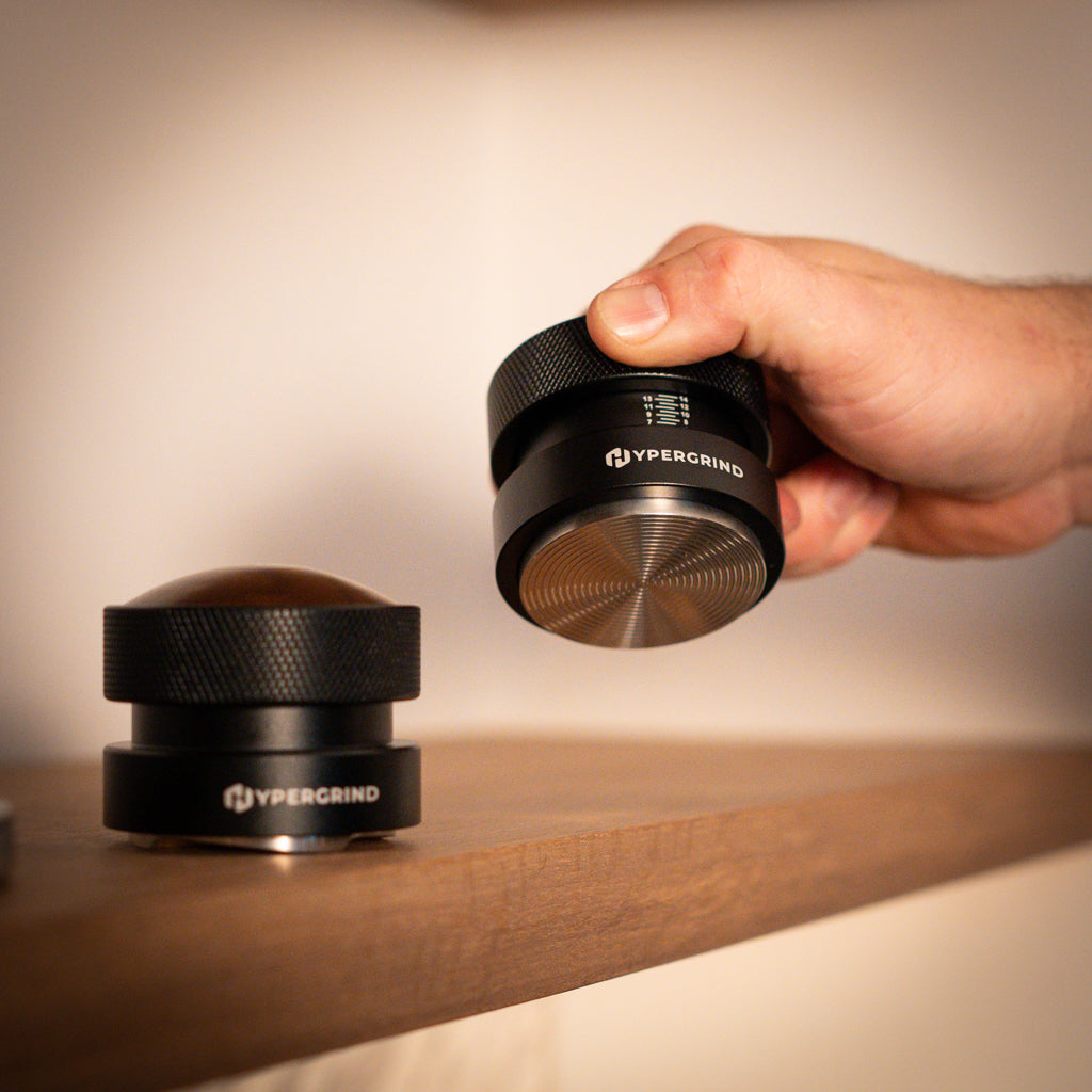 Hypergrind Gravity Distributor Tool (Black/Walnut) and palm tamper on a shelf